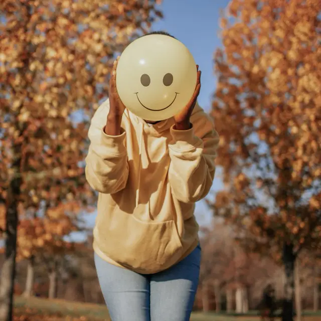 image d'une personne avec un ballon en forme d'emoji souriant devant son visage